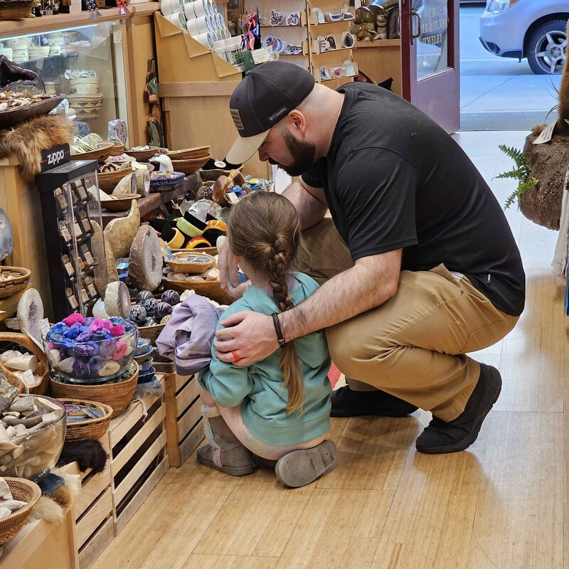 Jared crouched beside his daughter in a rock and mineral shop, looking at stones together
